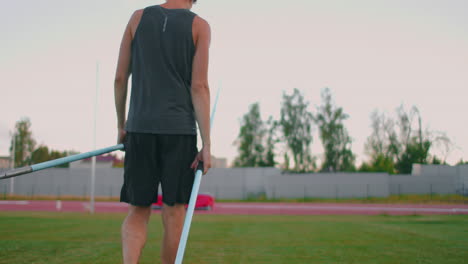Tired-javelin-thrower-a-man-at-the-stadium-collects-spears.-Preparing-for-the-all-around.-Walking-through-the-stadium-after-training-in-the-background-of-the-stands-and-carrying-spears-for-throwing.
